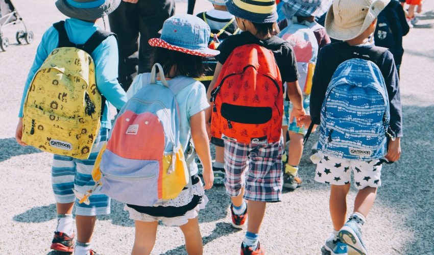 group of people wearing white and orange backpacks walking on gray concrete pavement during daytime